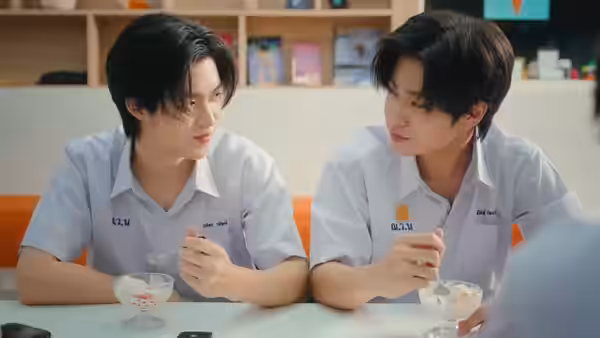 Two schoolboys share dessert at a table, leaning toward each other