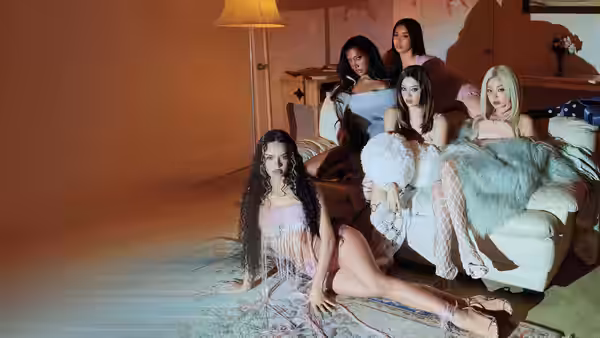 Five women pose together around a white sofa in a warmly lit room