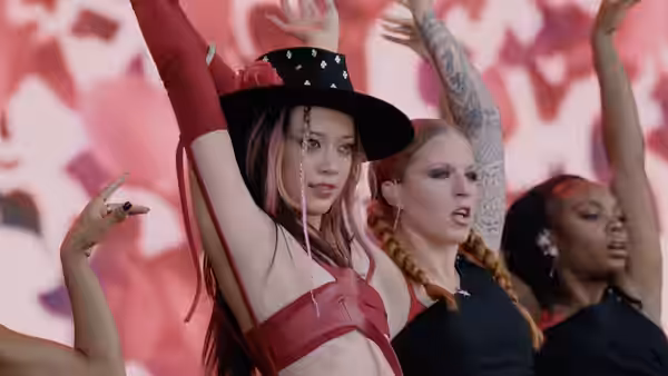 Three performers raise their arms onstage before a pink backdrop