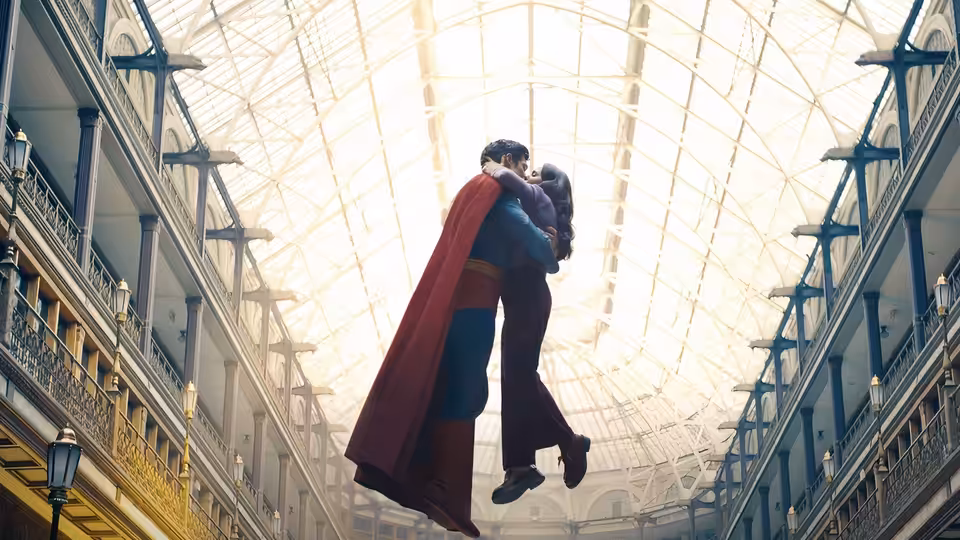 Superman (David Corenswet) holds Lois Lane (Rachel Brosnahan) while floating in a grand glass-roofed atrium