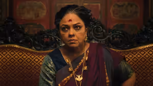 An older woman in a sari sits on an ornately carved sofa