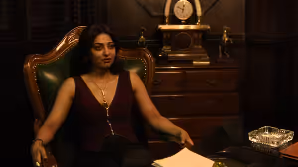 A woman sits at a desk beside papers and an ornate clock