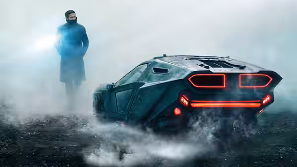 K (Ryan Gosling) stands beside a car with glowing red lights in fog