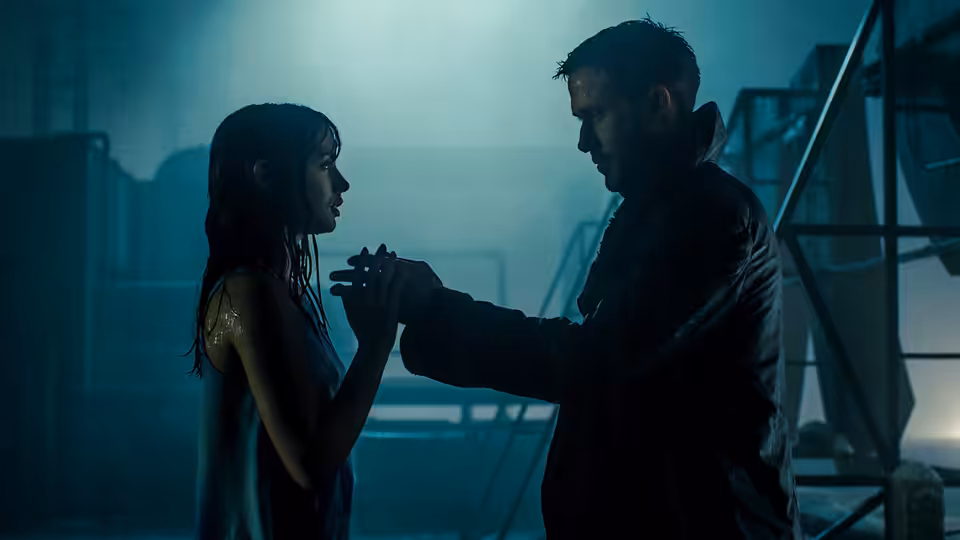 K (Ryan Gosling) and Joi (Ana de Armas) clasp hands in a misty industrial yard