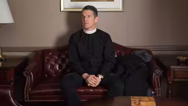 Pastor Toller (Ethan Hawke) seated on a red leather couch in clerical collar