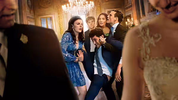 Wedding guests crowd together in the reception hall as a man bends forward