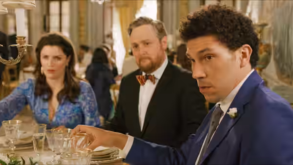 A wedding guest reaches across the dining table while two guests watch