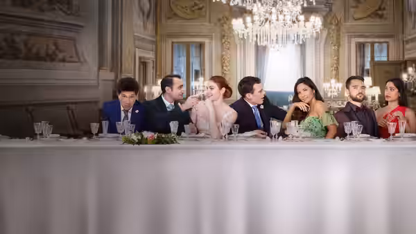 Wedding guests sit together at a long banquet table in an ornate reception hall
