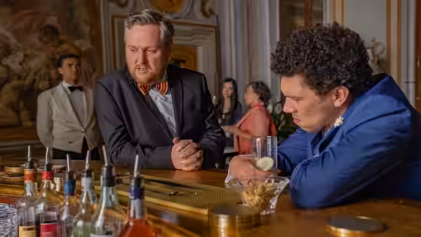 A man leans over the bar while another guest rests his head beside the drinks