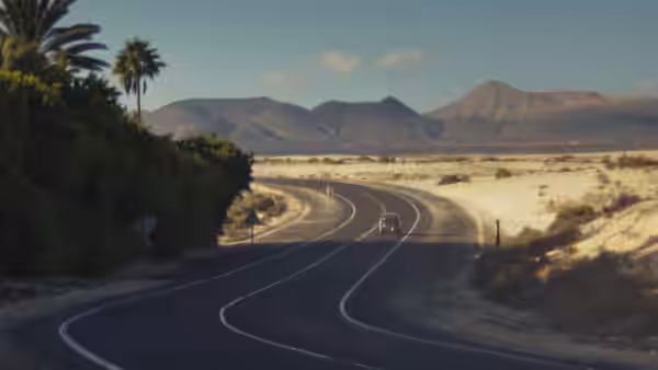 A winding road crosses a sandy landscape toward distant mountains