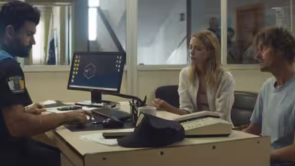 Tom (Sam Riley) and Anne (Stacy Martin) sit at a police station desk
