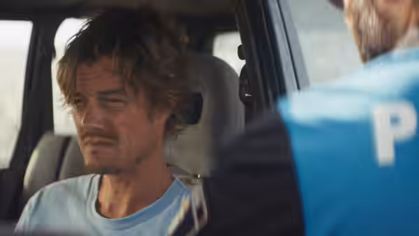 Tom (Sam Riley) sits inside a vehicle as a uniformed officer speaks to him