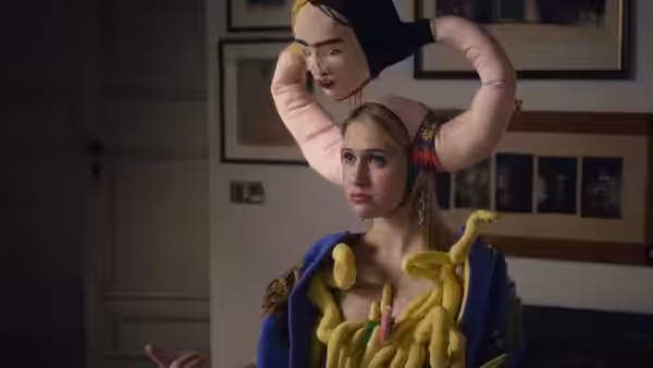 A woman in a blue outfit holds an oversized mask above her head