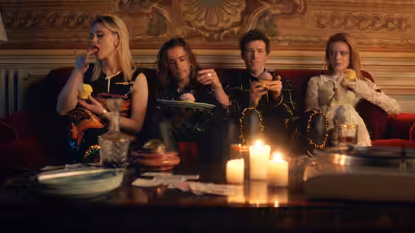 Four young adults sit on a velvet sofa eating at a candlelit table
