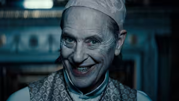 A man in a nightcap grins in a blue-lit room