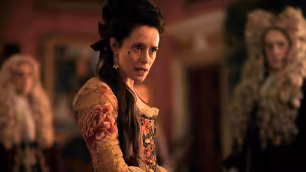 A woman in a floral gown looks back between two powdered-wig men indoors