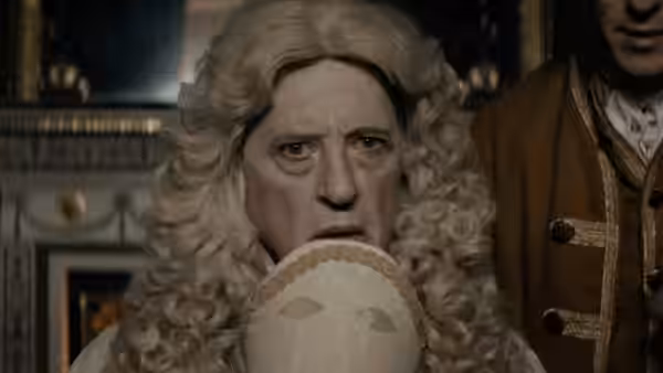 A powdered-wig man peers over a painted fan with a uniformed attendant behind him