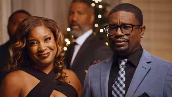 A woman and a bespectacled man stand together at a Christmas gathering