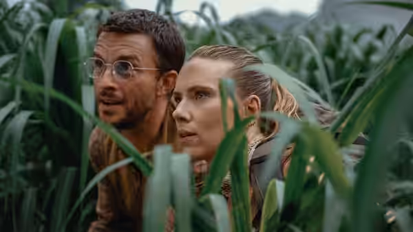 Zora Bennett (Scarlett Johansson) and Dr. Henry Loomis (Jonathan Bailey) peering through foliage