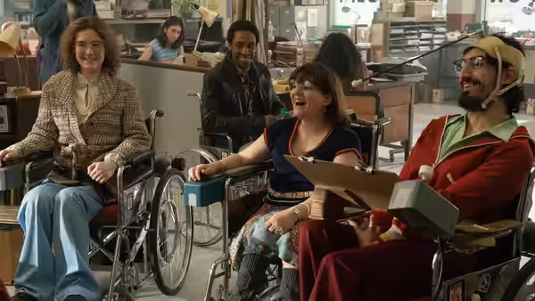 Wheelchair users gather around desks in an office, smiling and talking