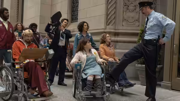 Wheelchair users gather outside a building as a police officer blocks the doorway