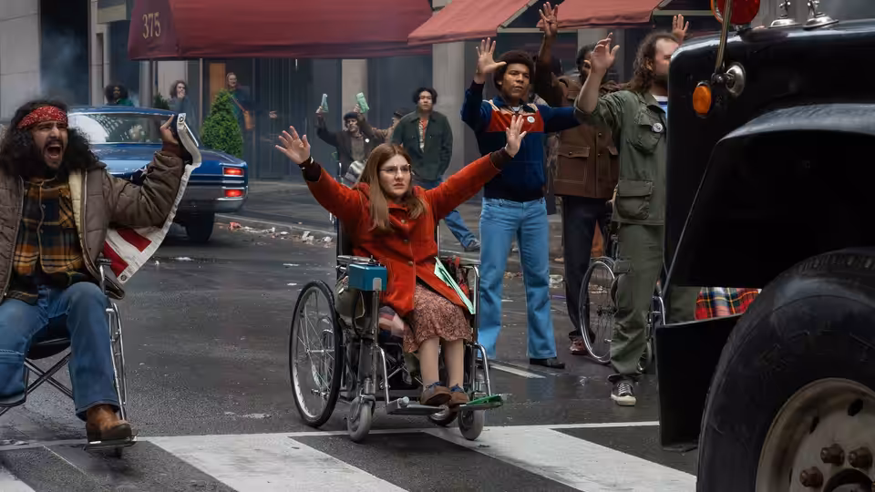 Judy Heumann (Ruth Madeley) and demonstrators raise their hands in the street