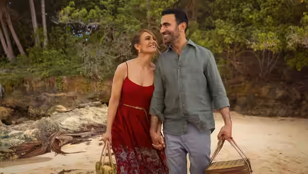 Jackie Cruz (Jennifer Lopez) and Daniel Blanchflower (Brett Goldstein) walk hand in hand along a wooded beach