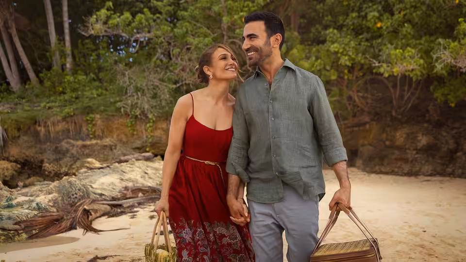 Jackie Cruz (Jennifer Lopez) and Daniel Blanchflower (Brett Goldstein) walk hand in hand along a wooded beach