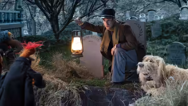 Gonzo and his dog peek from a grave as a man holds a lantern in the cemetery