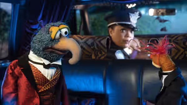 Gonzo and a red-haired puppet ride in a car with a uniformed driver