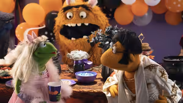 Miss Piggy, Fozzie and a guest gather around a Halloween party table