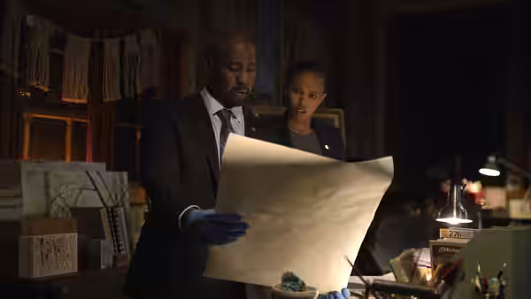 Erik Monks (D. B. Woodside) and a woman examine a large map in a study