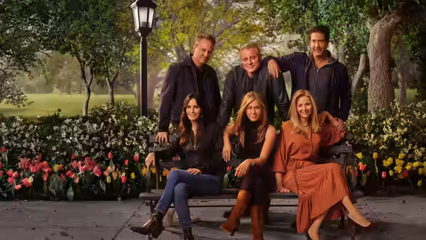The six Friends cast members pose together on a garden bench among flowers