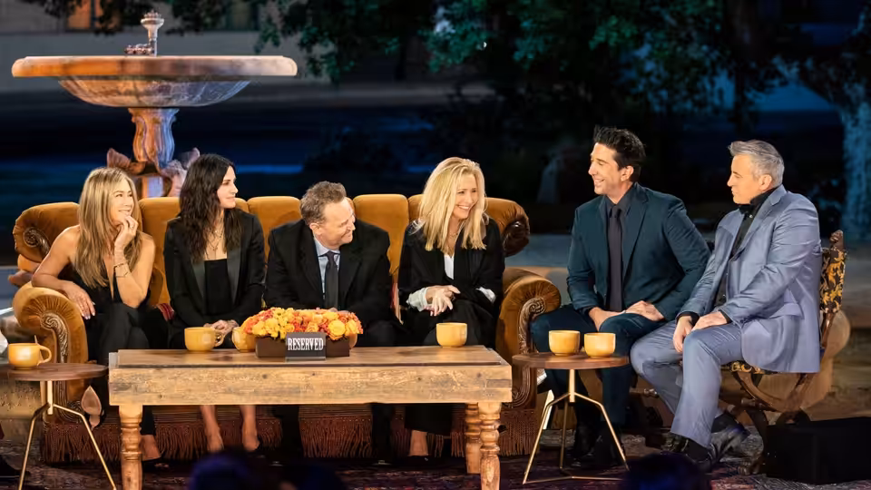 The six Friends cast members and James Corden sit together on the Central Perk set