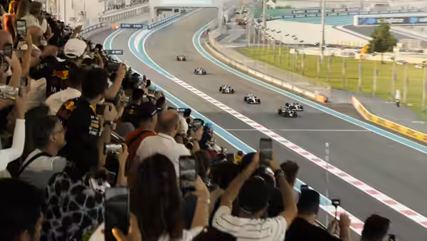 Spectators film Formula One cars racing around a track curve from the stands