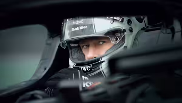 A driver in a green helmet looks ahead from inside a race car cockpit