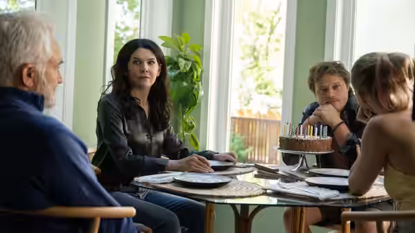 A family gathers around a dining table with a birthday cake