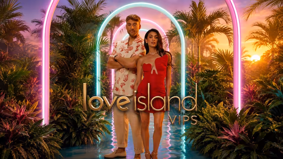 A man and woman pose beneath neon arches on a tropical garden walkway