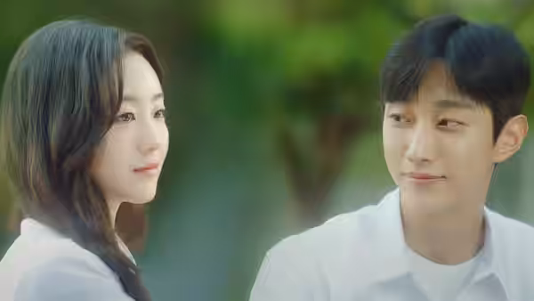 A young woman and man in white shirts sit outdoors, looking at each other