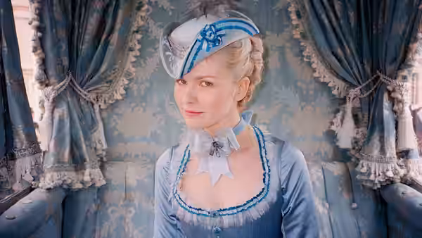 Marie Antoinette (Kirsten Dunst) stands before patterned curtains in a blue gown