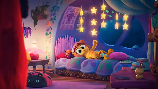 A small bird lounges beside an orange cat on a colorful bedroom bed