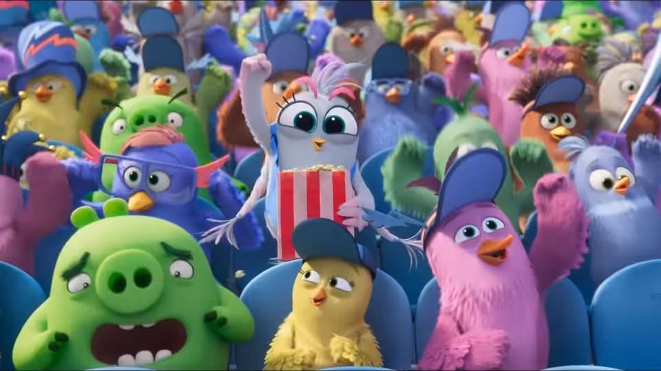 Birds and pigs cheer from packed seats as a small bird in a striped shirt raises its wings