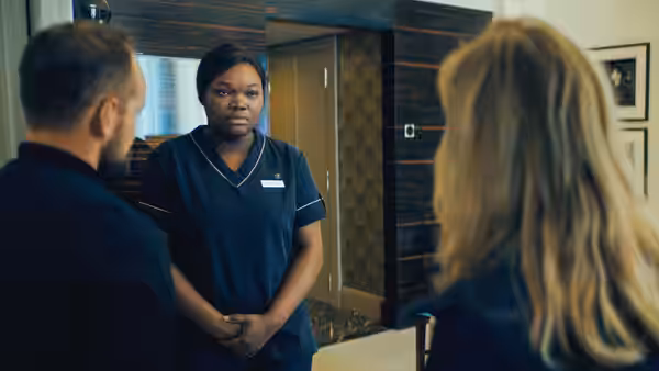 A nurse in navy scrubs faces two visitors in a reception area