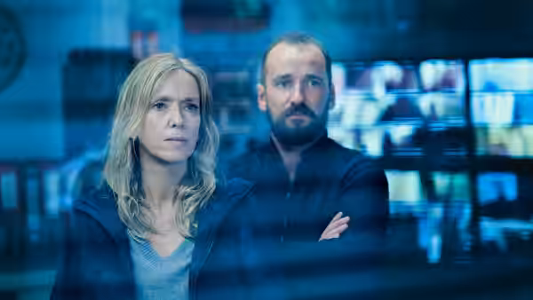 Stéphanie Bertrand (Léa Drucker) and a bearded colleague stand before glowing surveillance monitors