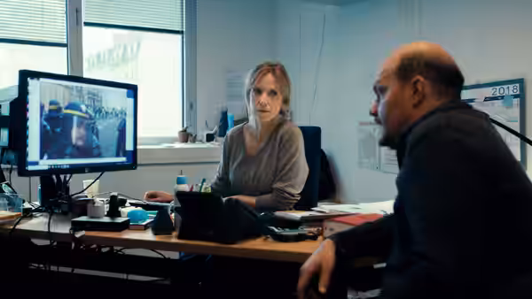 Stéphanie Bertrand (Léa Drucker) sits at her desk beside a colleague, with a monitor showing footage