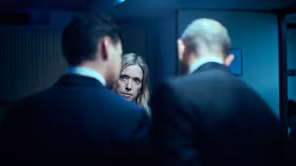 Stéphanie Bertrand (Léa Drucker) looks between two suited men in a dim corridor