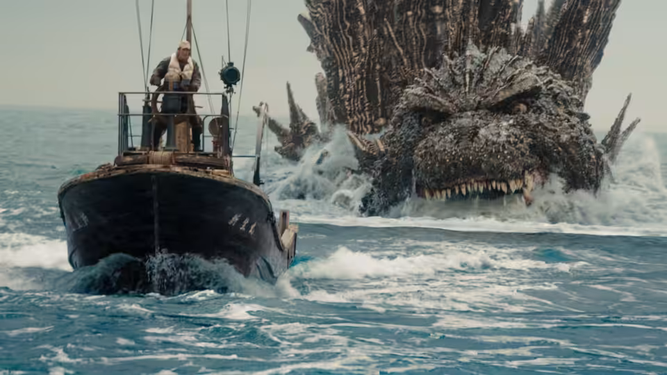 A man on a boat faces Godzilla rising from the sea