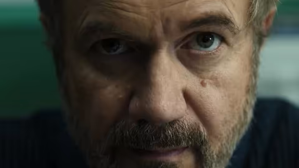 A bearded man looks directly ahead, his face filling the frame