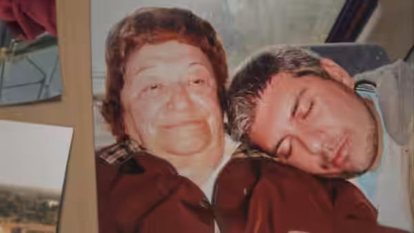An older woman smiles while a man rests his head on her shoulder