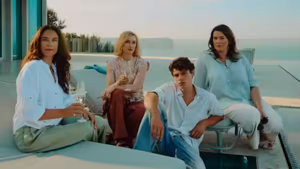 Three women and a young man sit beside a swimming pool at a modern house